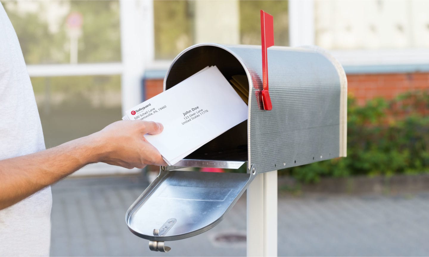 A person putting addressed letters into a mailbox outside.