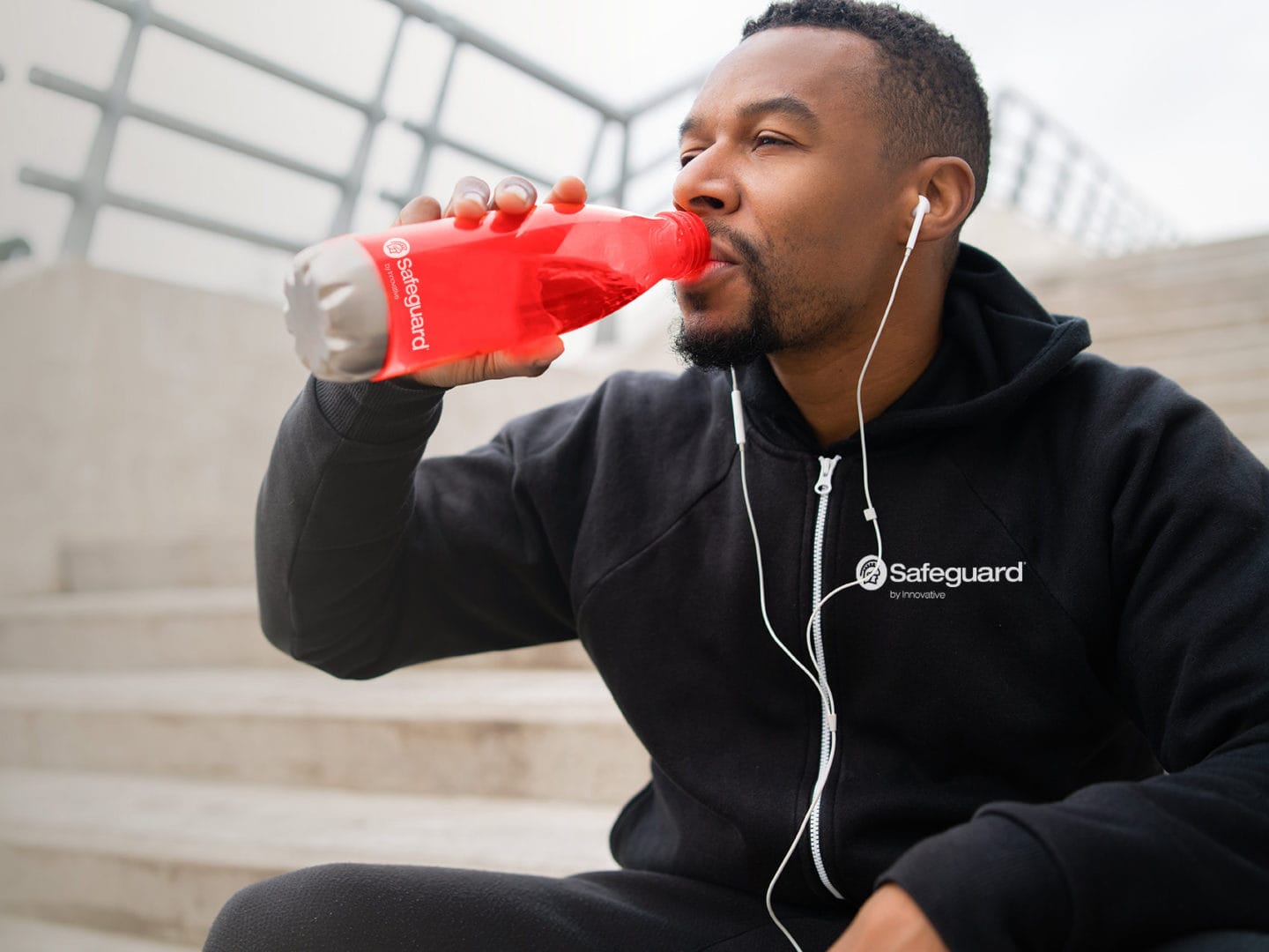 Man sitting on stairs outside drinking out of a red Safeguard branded water bottle.
