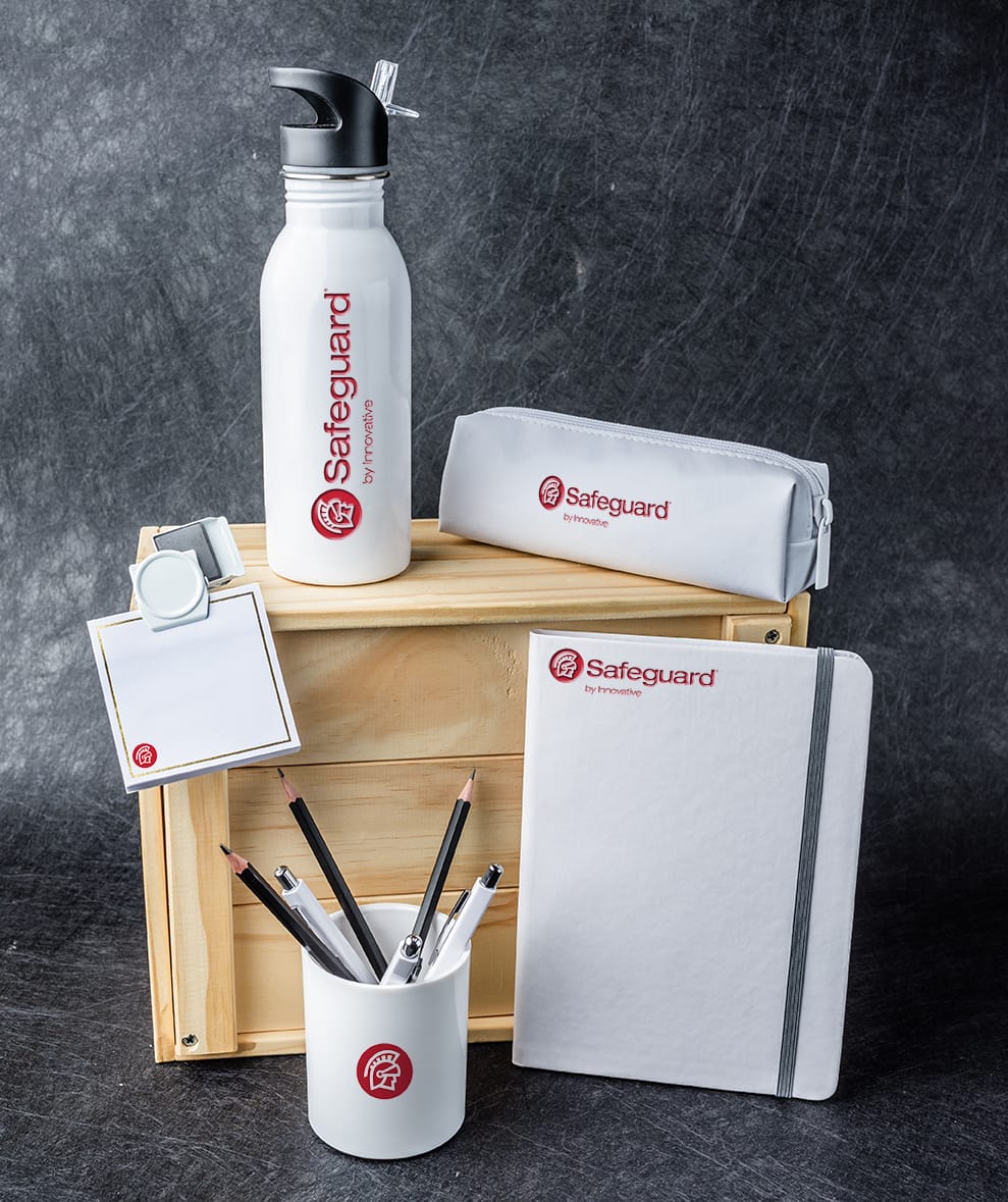 Safeguard promotional items arranged around a wooden box: Pens, a mug, a notebook, a water bottle, etc.