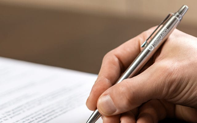 A hand holding a Safeguard by Innovative branded pen and writing on paper.