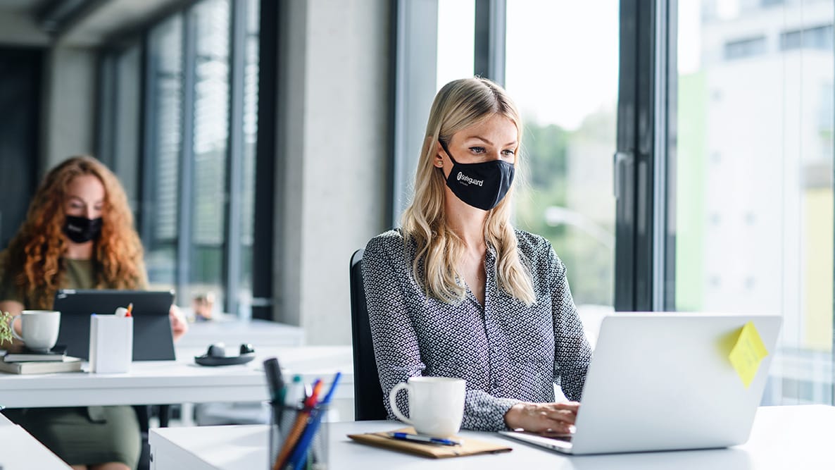 Woman wearing a Safeguard face mask while working on her laptop in an office.