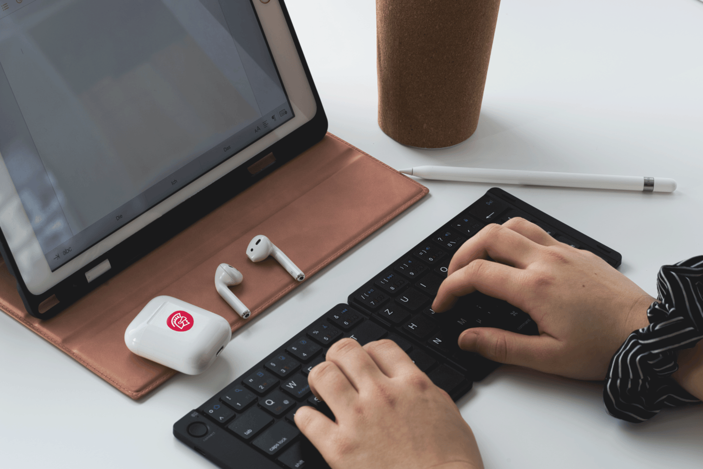 A person types on a keyboard in front of an iPad while Safeguard branded Airpods lay in front of it.