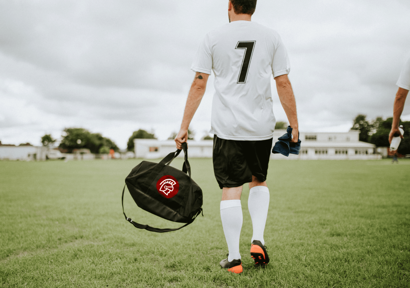 Two soccer players walk away across a field while carrying a Safeguard branded duffle bag.