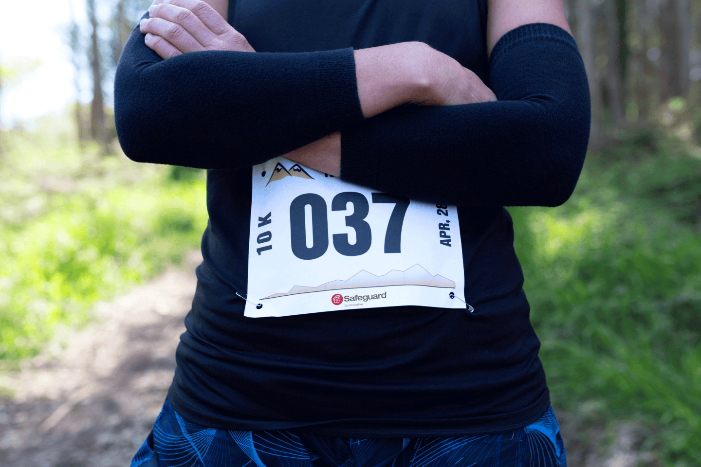 A 10K runner standing outside in the woods with their arms crossed while wearing the number 037.
