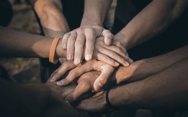 A group of people placing their hands together on top of each other in a team huddle.
