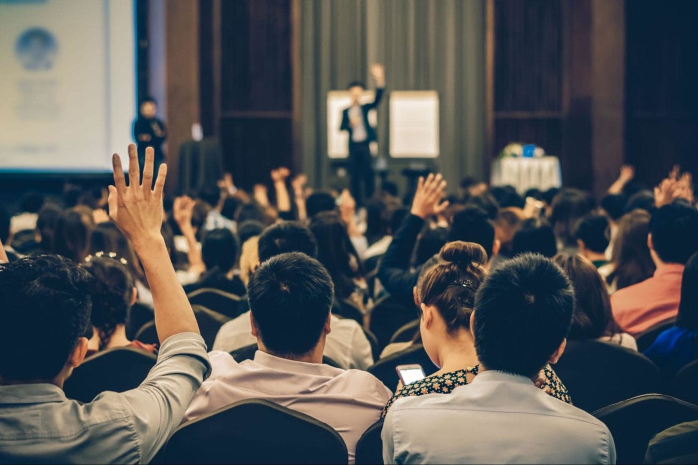 Hands raised in a crowd at a presentation.