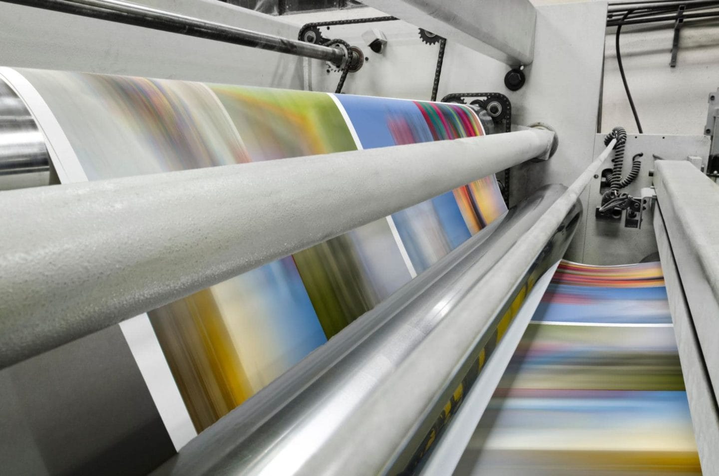 A picture of a commercial printer printing large sheets of paper with vibrant colors.