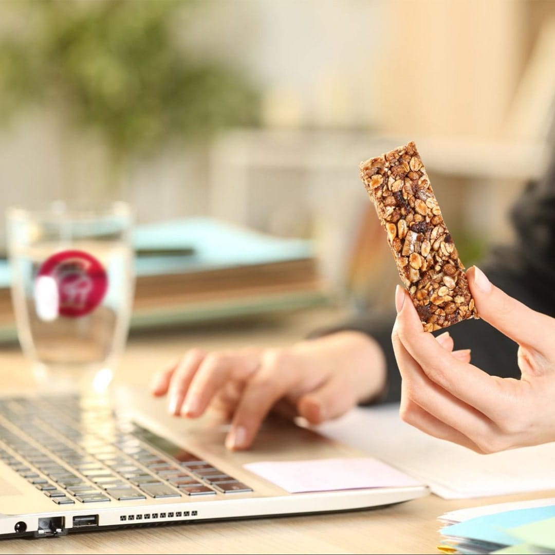 A person eating a granola bar at their desk.