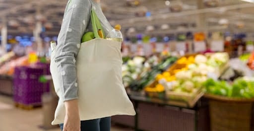 A woman grocery shopping with a reusable bag because of plastic bag bans.