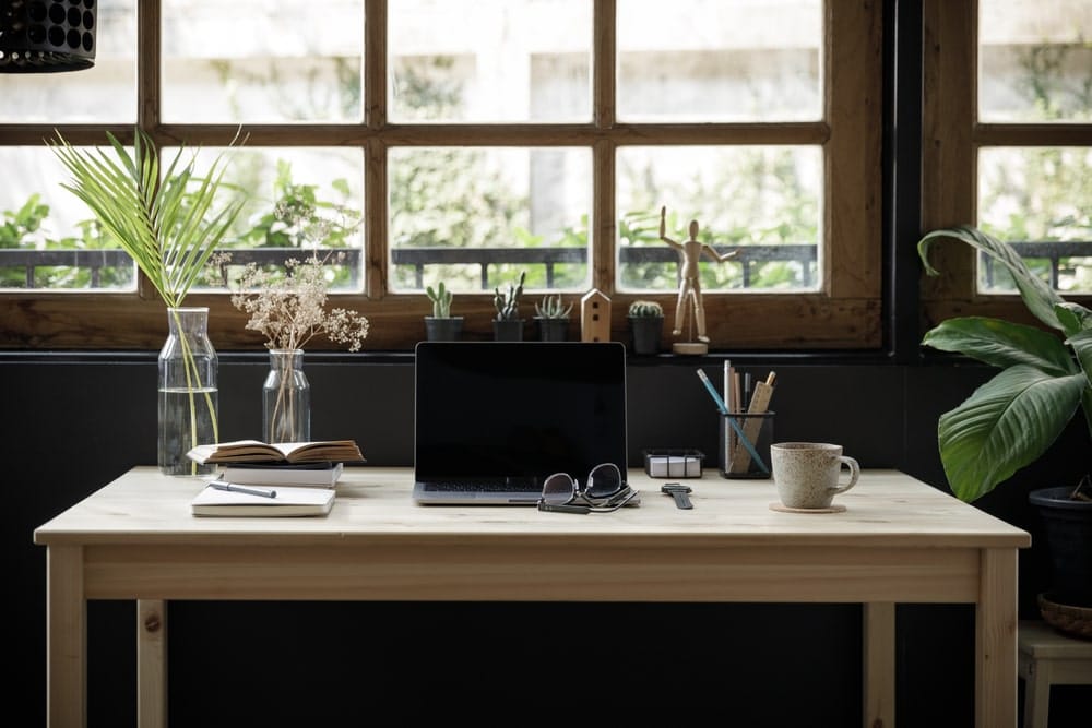 A wooden work from home desk setup with plants, a laptop, and other home office essentials.
