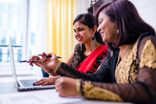 Two women sitting smiling and looking at a laptop while designing a logo.