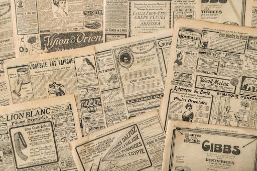 An assortment of old newspapers showing ads.