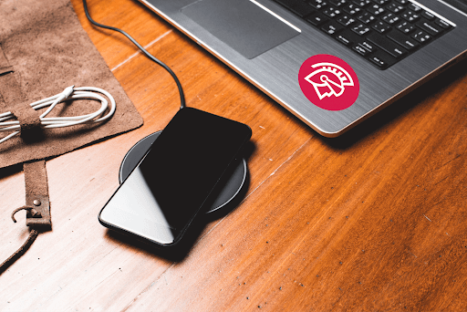 A phone charges on a wireless charger next to a laptop with a custom Safeguard by Innovative sticker on it.