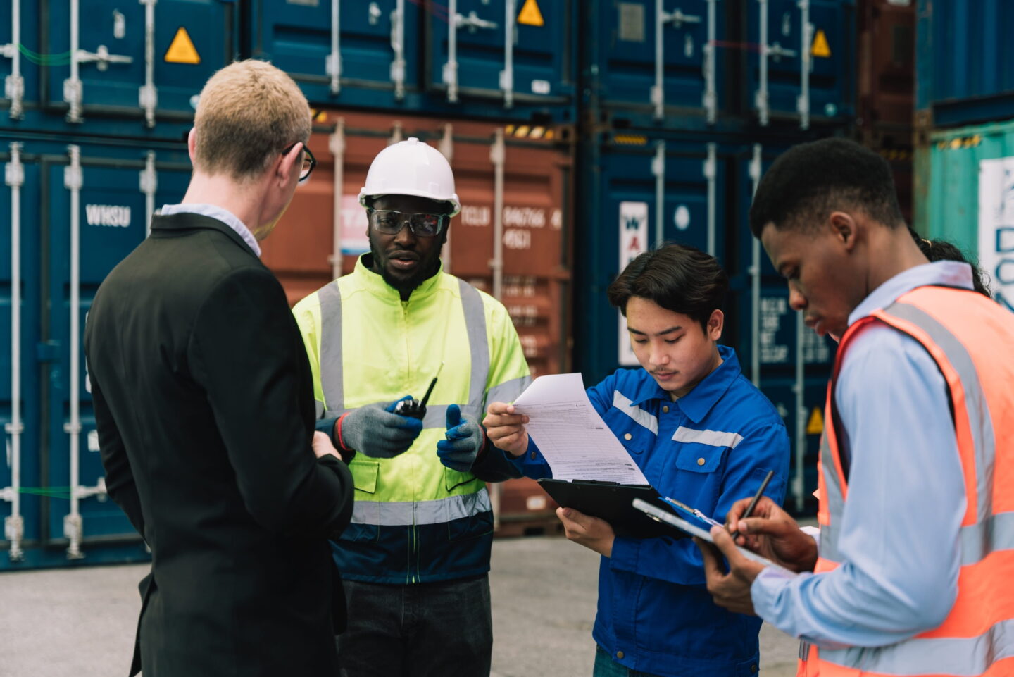 Business person, dock workers, and inspector discussing shipping on a dock.