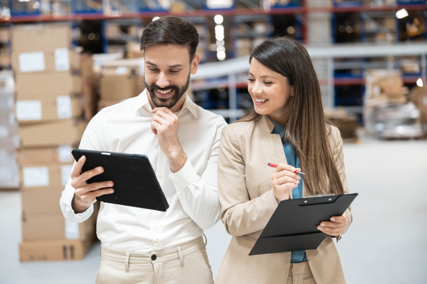 A procurement leader and a label print partner smiling while reviewing production details on a tablet in a warehouse setting.